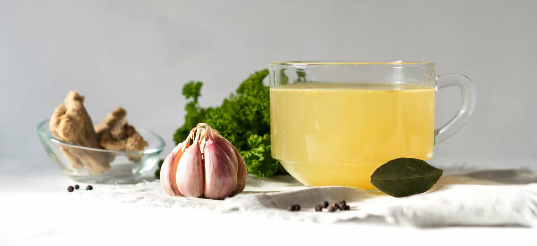 Collagen broth in a glass, and next to it garlic, vegetables and spices.