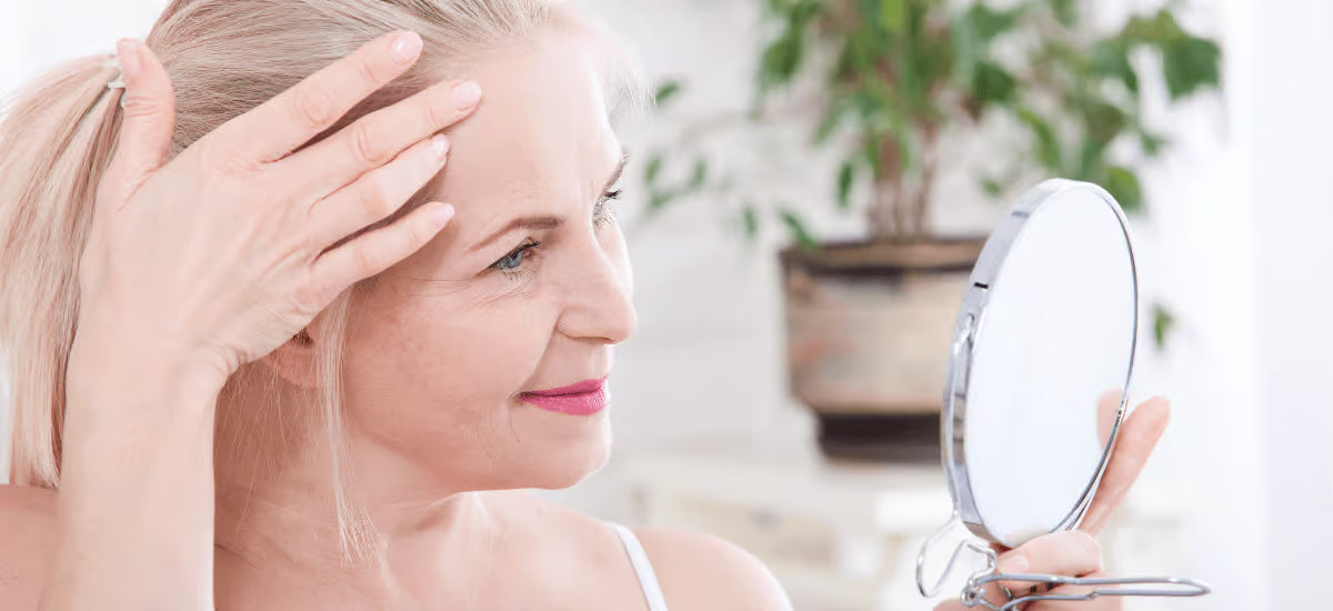 A smiling middle-aged woman looking at herself in the mirror at her wrinkles.
