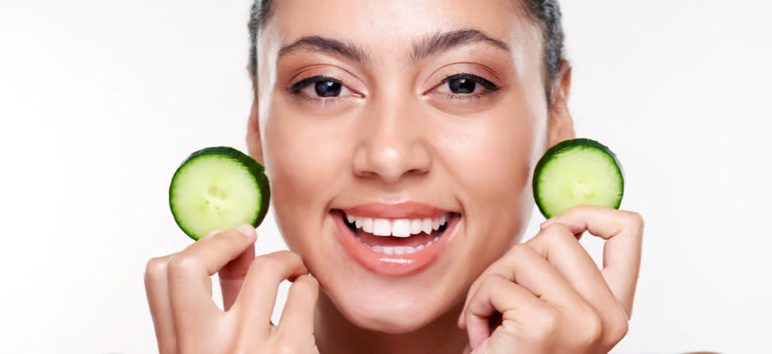 A smiling woman with healthy-looking skin holding cucumber slices.