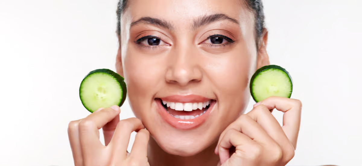 A smiling woman with healthy-looking skin holding cucumber slices.