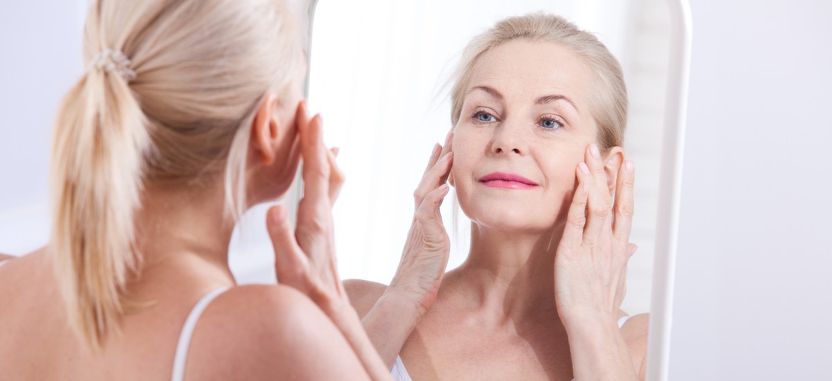 Mature woman touching her face and looking in the mirror with a gentle smile