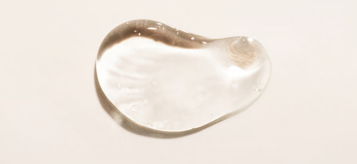 Close-up of a clear drop of hyaluronic acid with a smooth, glossy texture on a neutral background