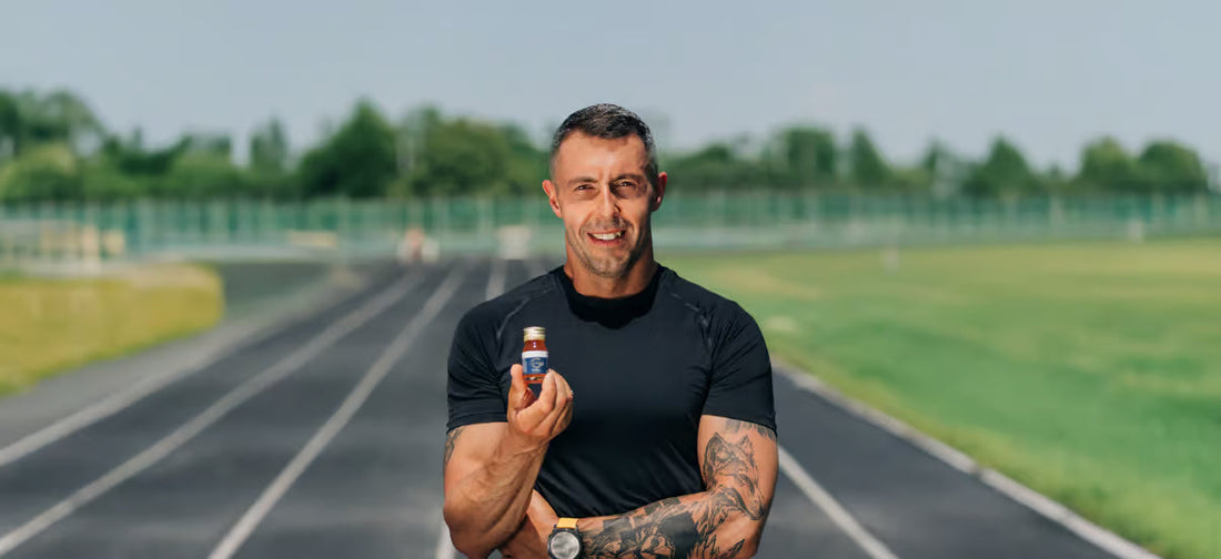 The smiling world record holder in 10x Ironman, Jurand Czabański, stands on the running track holding Collagen Sport from Primabiotic in his hand