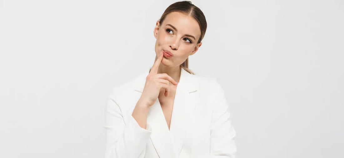 A woman with dark tied-up hair wearing a white suit against a white background with a pensive expression on her face