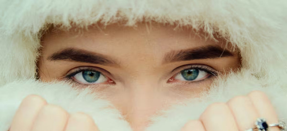 Close-up of blue-eyed woman wrapped in soft white fur, protecting her winter-sensitive skin.