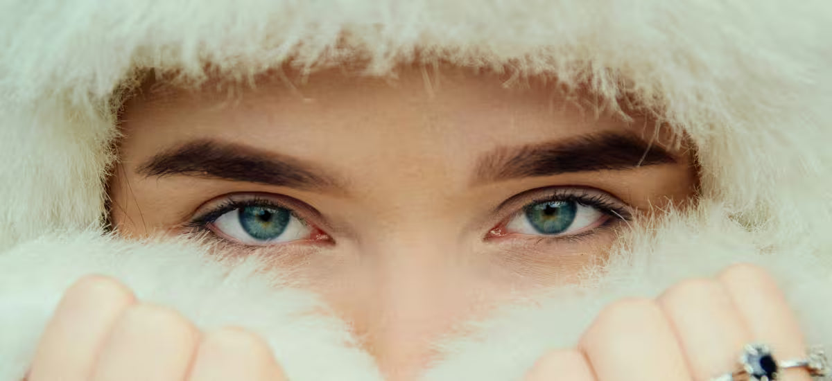 Close-up of blue-eyed woman wrapped in soft white fur, protecting her winter-sensitive skin.