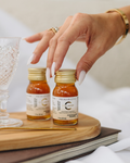 Hand reaches for Primabiotic Collagen shot, small bottles placed on a wooden tray